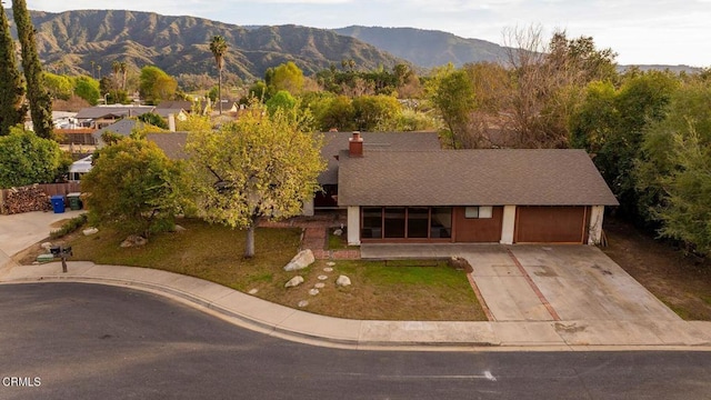 view of front of property with driveway, a chimney, an attached garage, a mountain view, and a front yard