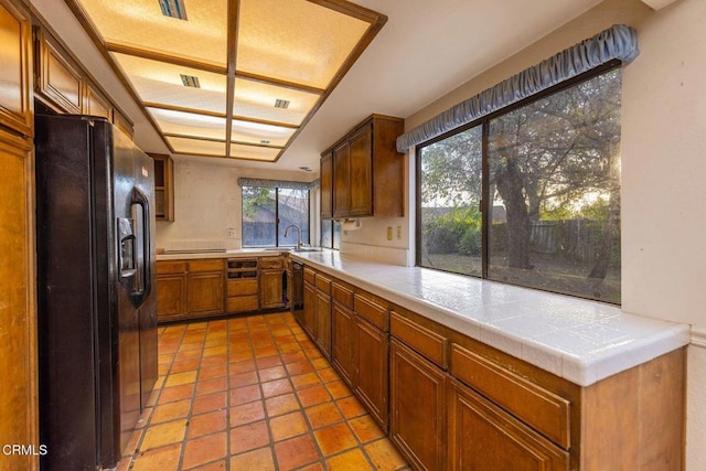 kitchen featuring brown cabinetry, dishwasher, light countertops, black fridge, and a sink