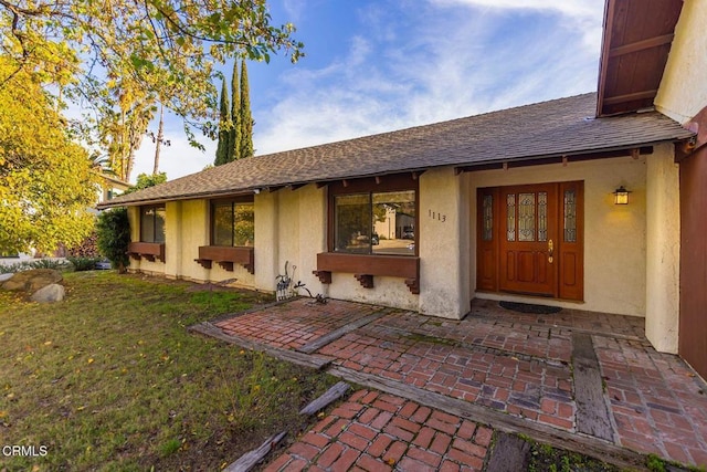 rear view of house with roof with shingles, a lawn, and stucco siding