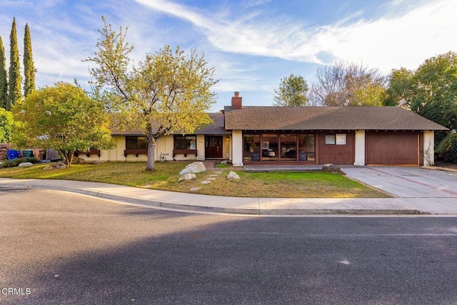 ranch-style home with an attached garage, driveway, a chimney, and a front lawn