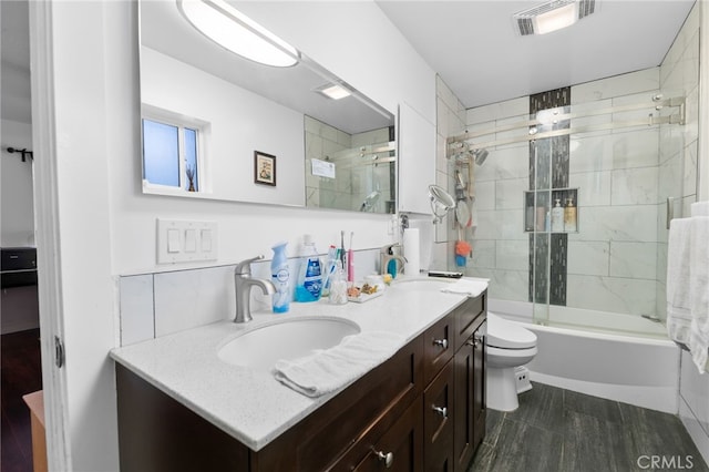 full bathroom with double vanity, visible vents, toilet, shower / bath combination with glass door, and a sink