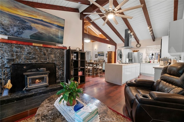 living area featuring dark wood-style flooring, ceiling fan, a lit fireplace, and beam ceiling