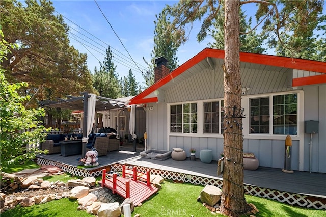 back of property featuring board and batten siding, a chimney, an outdoor living space, and a wooden deck