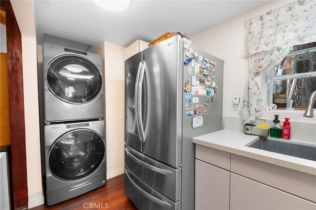 laundry area featuring stacked washing maching and dryer, laundry area, dark wood finished floors, and a sink