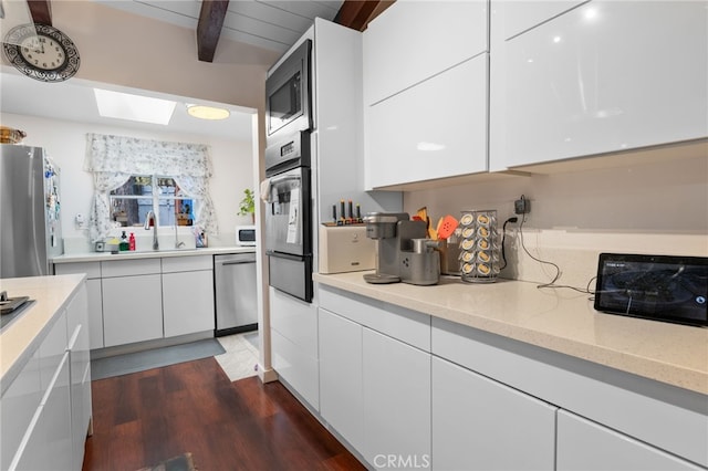 kitchen featuring beam ceiling, a warming drawer, stainless steel appliances, white cabinets, and a sink