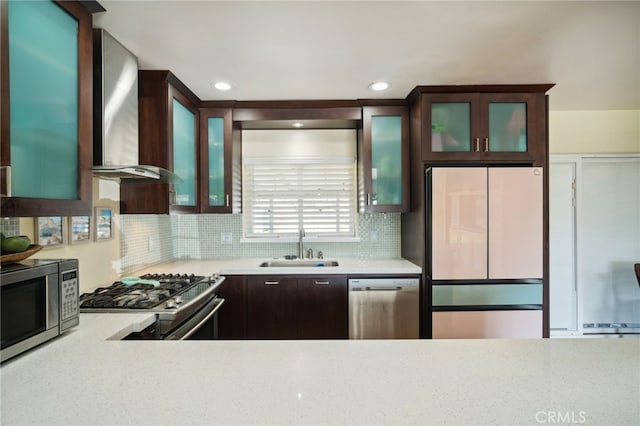 kitchen featuring dark brown cabinetry, wall chimney exhaust hood, stainless steel appliances, light countertops, and a sink