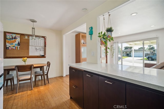 kitchen featuring light wood finished floors, light stone counters, decorative light fixtures, dark brown cabinets, and recessed lighting