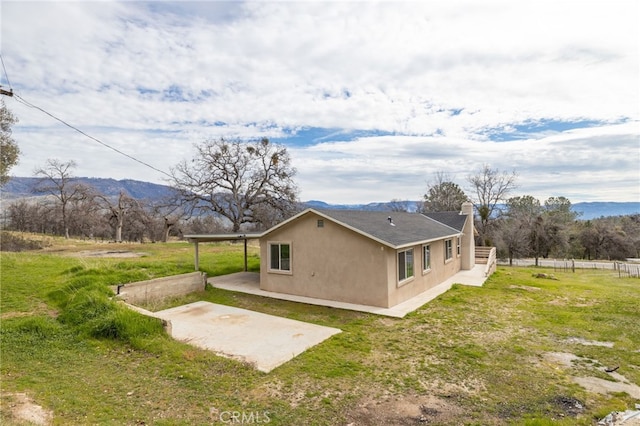 view of side of home with a mountain view, fence, a yard, stucco siding, and a patio area