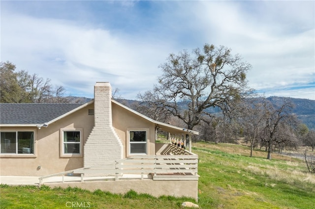 rear view of property featuring a shingled roof, a chimney, and stucco siding