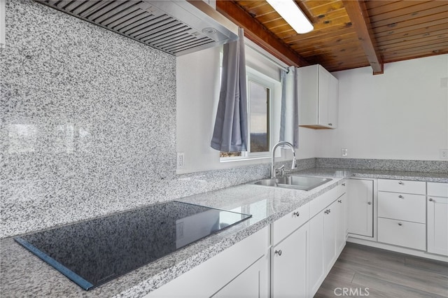 kitchen with beamed ceiling, range hood, black electric stovetop, white cabinetry, and a sink