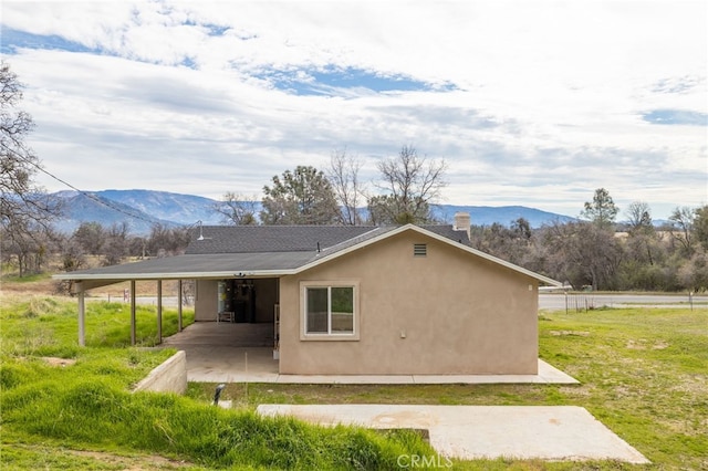 rear view of property featuring a lawn, a mountain view, a patio, and stucco siding