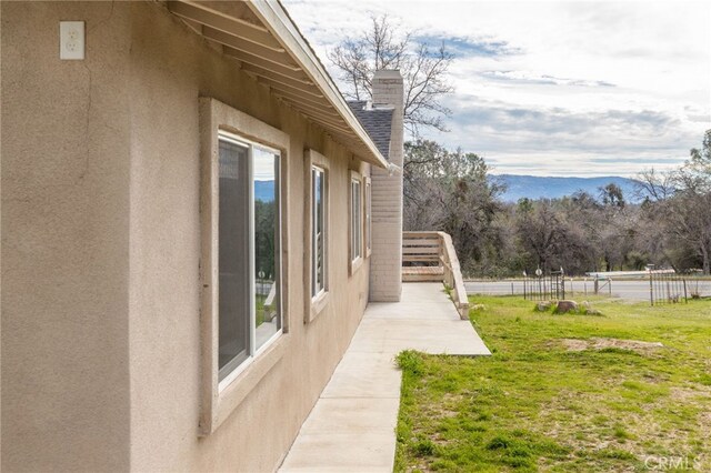 view of home's exterior with a chimney, fence, a yard, stucco siding, and a patio