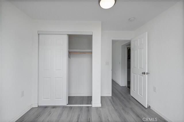 unfurnished bedroom featuring baseboards, wood finished floors, and a closet