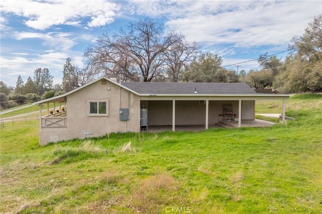 rear view of house featuring a lawn and stucco siding