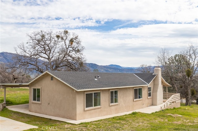 back of property featuring a chimney, stucco siding, a shingled roof, a lawn, and a mountain view