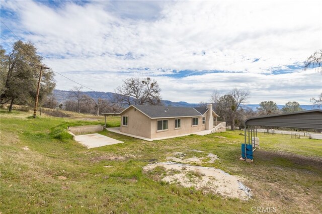 back of property featuring stucco siding, a patio area, a carport, a lawn, and a mountain view