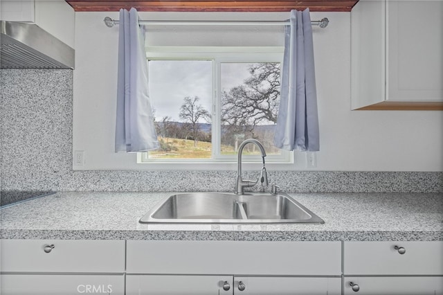 kitchen featuring light countertops, a sink, white cabinetry, and under cabinet range hood