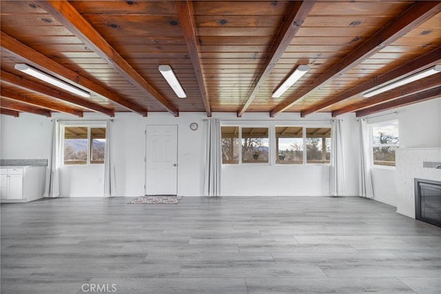 unfurnished living room with a brick fireplace, beam ceiling, and wood finished floors