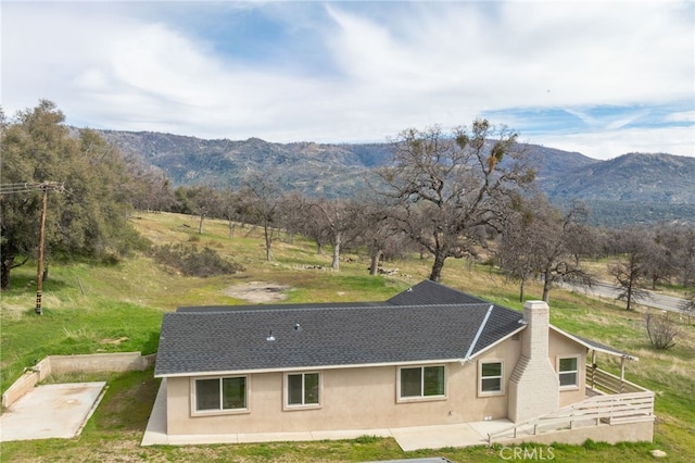 exterior space with roof with shingles, a chimney, stucco siding, a patio area, and a mountain view