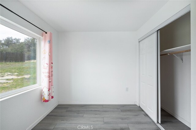 unfurnished bedroom featuring baseboards, wood finished floors, and a closet