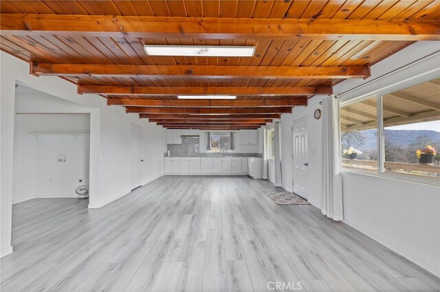unfurnished living room featuring wooden ceiling, beamed ceiling, a mountain view, baseboards, and light wood-style flooring