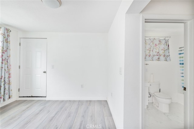 interior space with light wood-style floors, ensuite bath, and baseboards