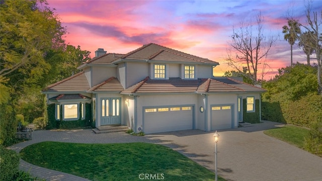 view of front of property with a tiled roof, decorative driveway, a chimney, and an attached garage