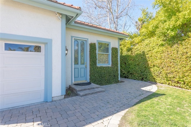 doorway to property featuring an attached garage, a tile roof, and stucco siding