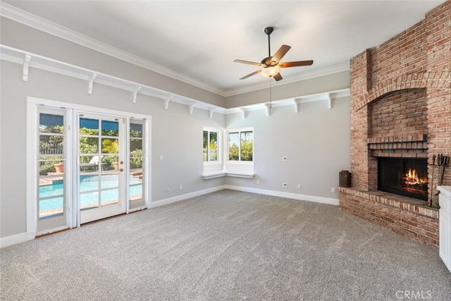 unfurnished living room with ornamental molding, a brick fireplace, carpet flooring, ceiling fan, and baseboards