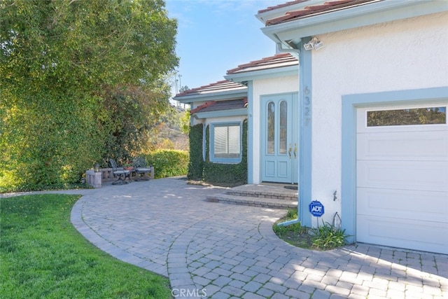 doorway to property with a garage, a tile roof, and stucco siding