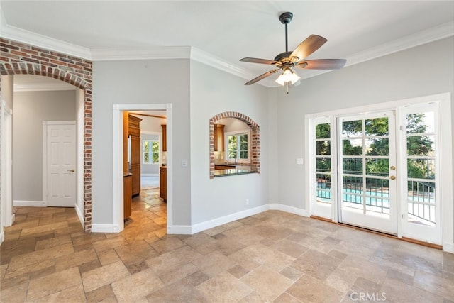 unfurnished room with stone tile floors, baseboards, arched walkways, and crown molding