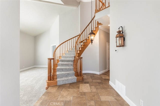 staircase with a towering ceiling, baseboards, visible vents, and stone tile flooring