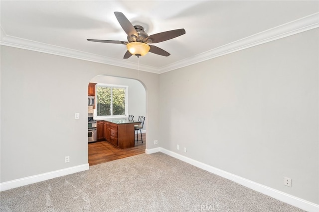 unfurnished room featuring arched walkways, carpet floors, baseboards, and crown molding