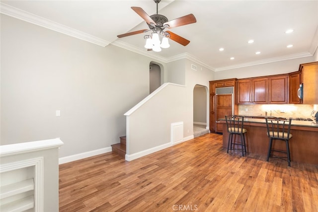 kitchen with arched walkways, a breakfast bar area, backsplash, ornamental molding, and light wood-type flooring