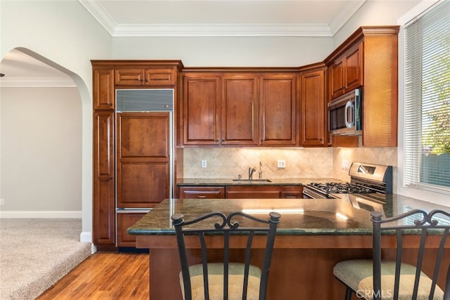 kitchen with arched walkways, dark stone counters, a peninsula, stainless steel appliances, and a sink