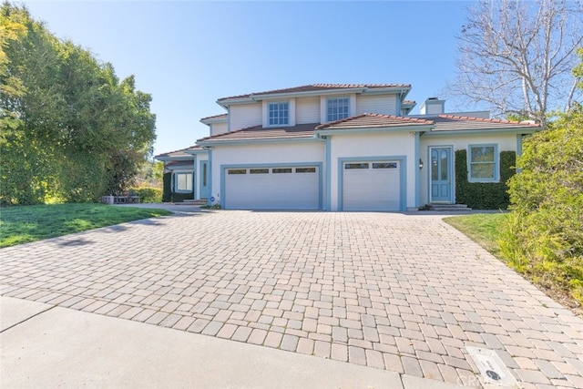 view of front facade with decorative driveway, a tile roof, a chimney, stucco siding, and an attached garage