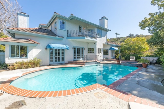 back of house featuring french doors, a patio area, a chimney, and a balcony