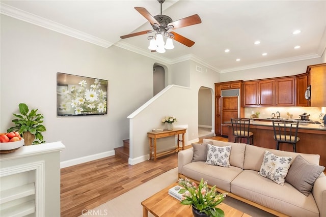 living area featuring light wood-style flooring, stairs, arched walkways, and ornamental molding