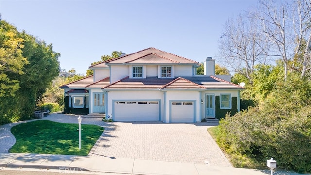 view of front of house featuring a front yard, decorative driveway, a tiled roof, and an attached garage