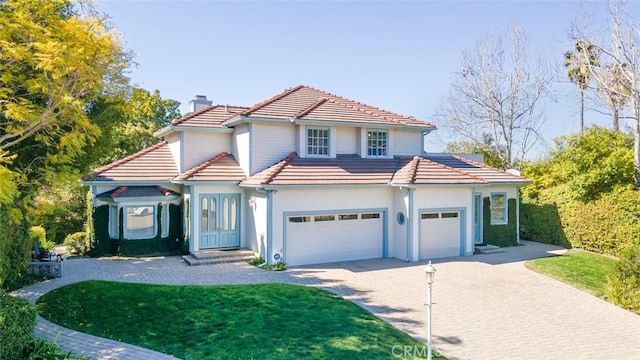 mediterranean / spanish-style house with a garage, driveway, a tile roof, and a chimney