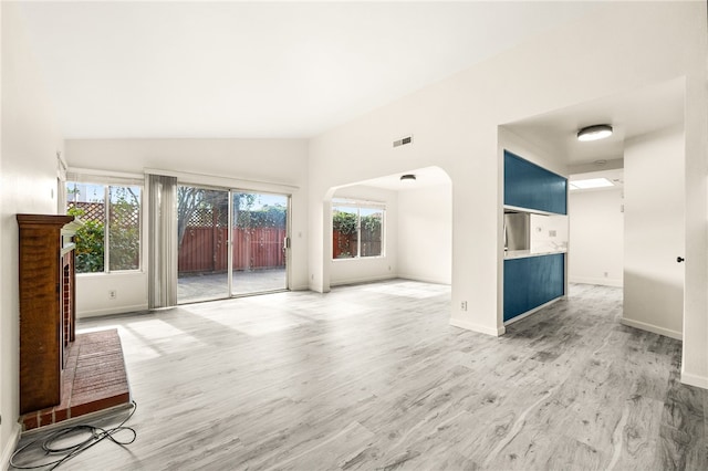 unfurnished living room with light wood-type flooring, visible vents, lofted ceiling, and baseboards