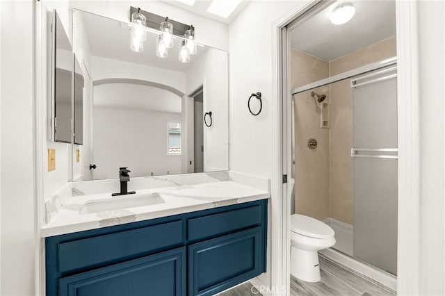 bathroom featuring wood finished floors, toilet, a stall shower, and vanity