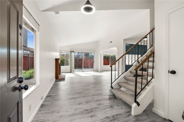 foyer featuring baseboards, wood finished floors, stairs, and vaulted ceiling