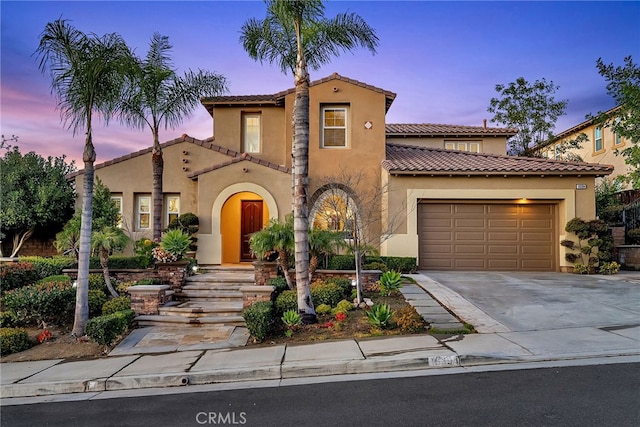 mediterranean / spanish home with a garage, a tiled roof, concrete driveway, and stucco siding