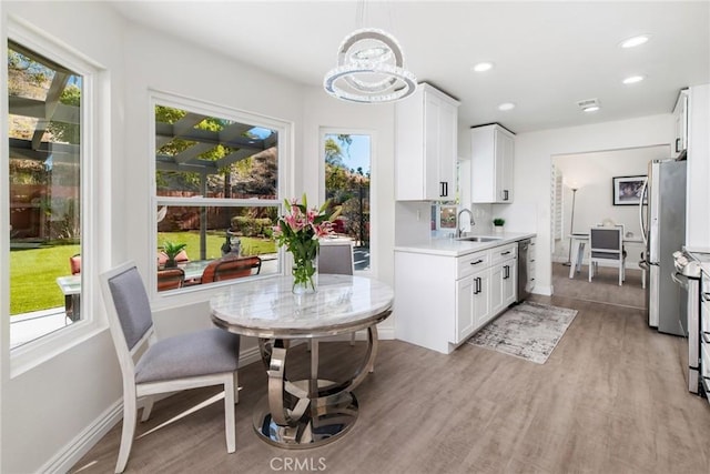 kitchen featuring light wood-style flooring, stainless steel appliances, light countertops, white cabinetry, and a sink