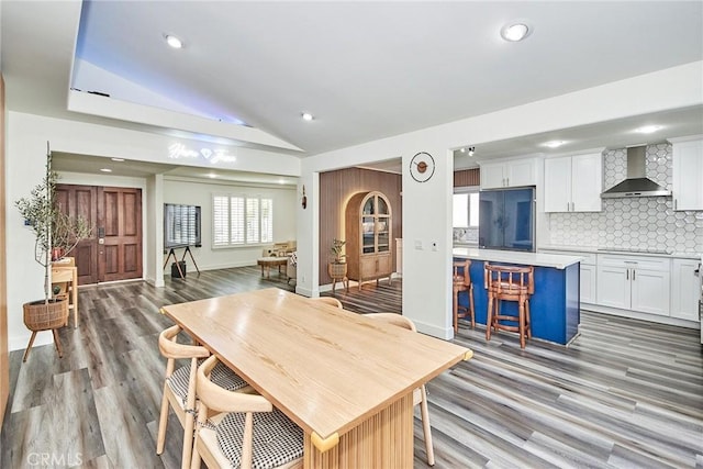 kitchen featuring lofted ceiling, wall chimney range hood, white cabinets, and light countertops