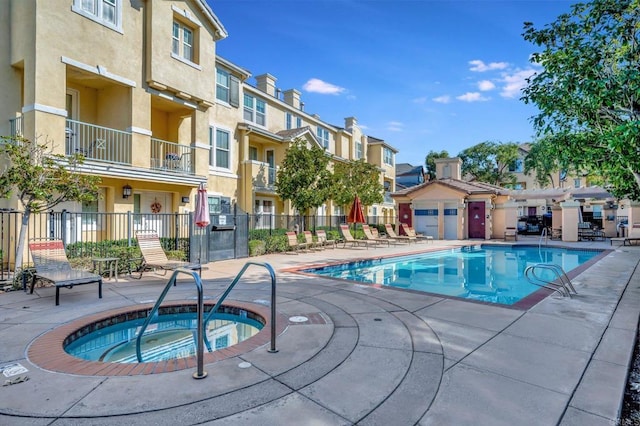 pool featuring a community hot tub, a patio area, fence, and a residential view