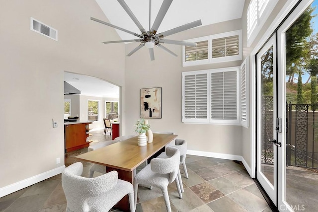 dining space featuring arched walkways, a towering ceiling, visible vents, and baseboards