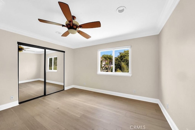 unfurnished bedroom featuring a ceiling fan, crown molding, baseboards, and wood finished floors