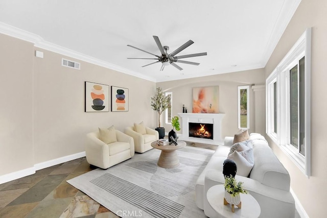 living room featuring a warm lit fireplace, baseboards, visible vents, ceiling fan, and ornamental molding